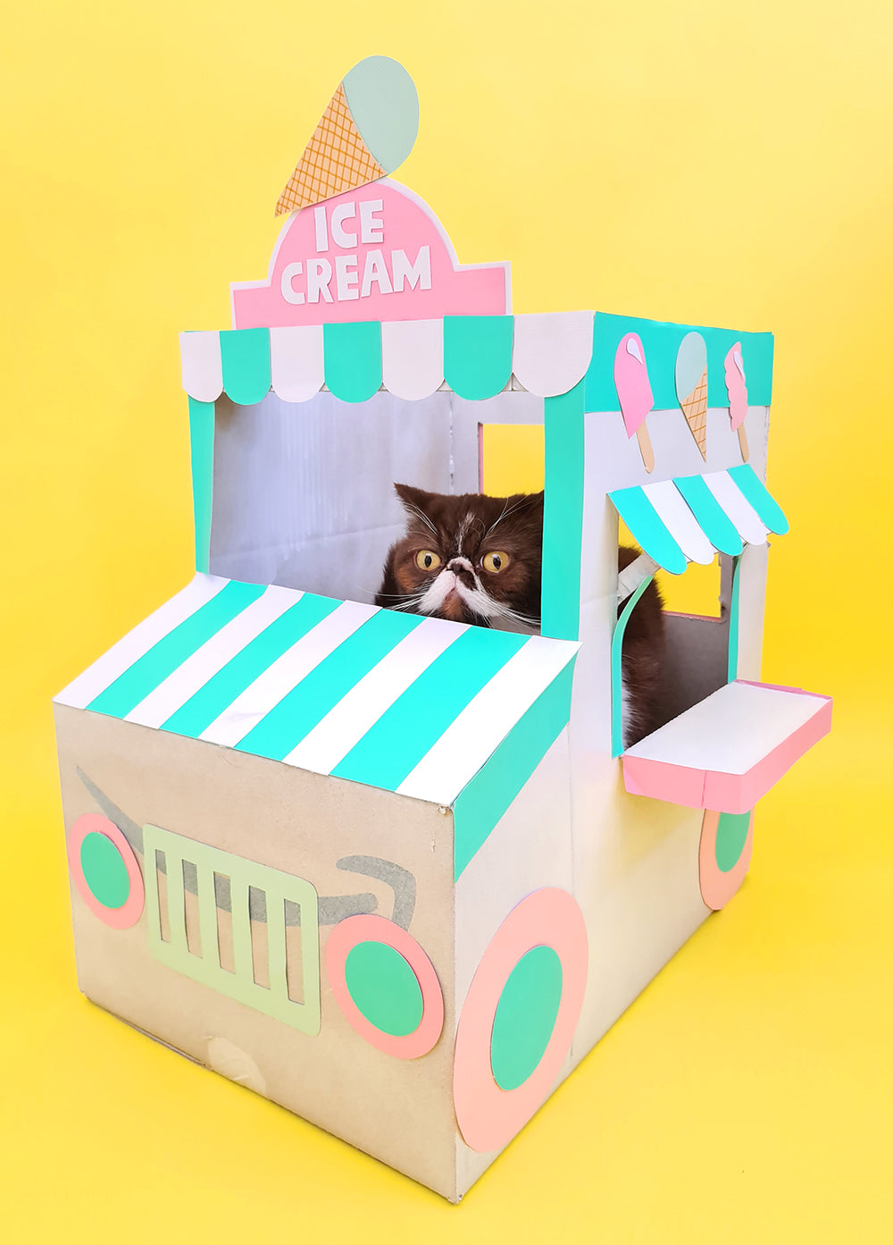 On a yellow background sits a pink, white and green painted 'boxtume' of an icecream truck created by Kitiya Palaskas