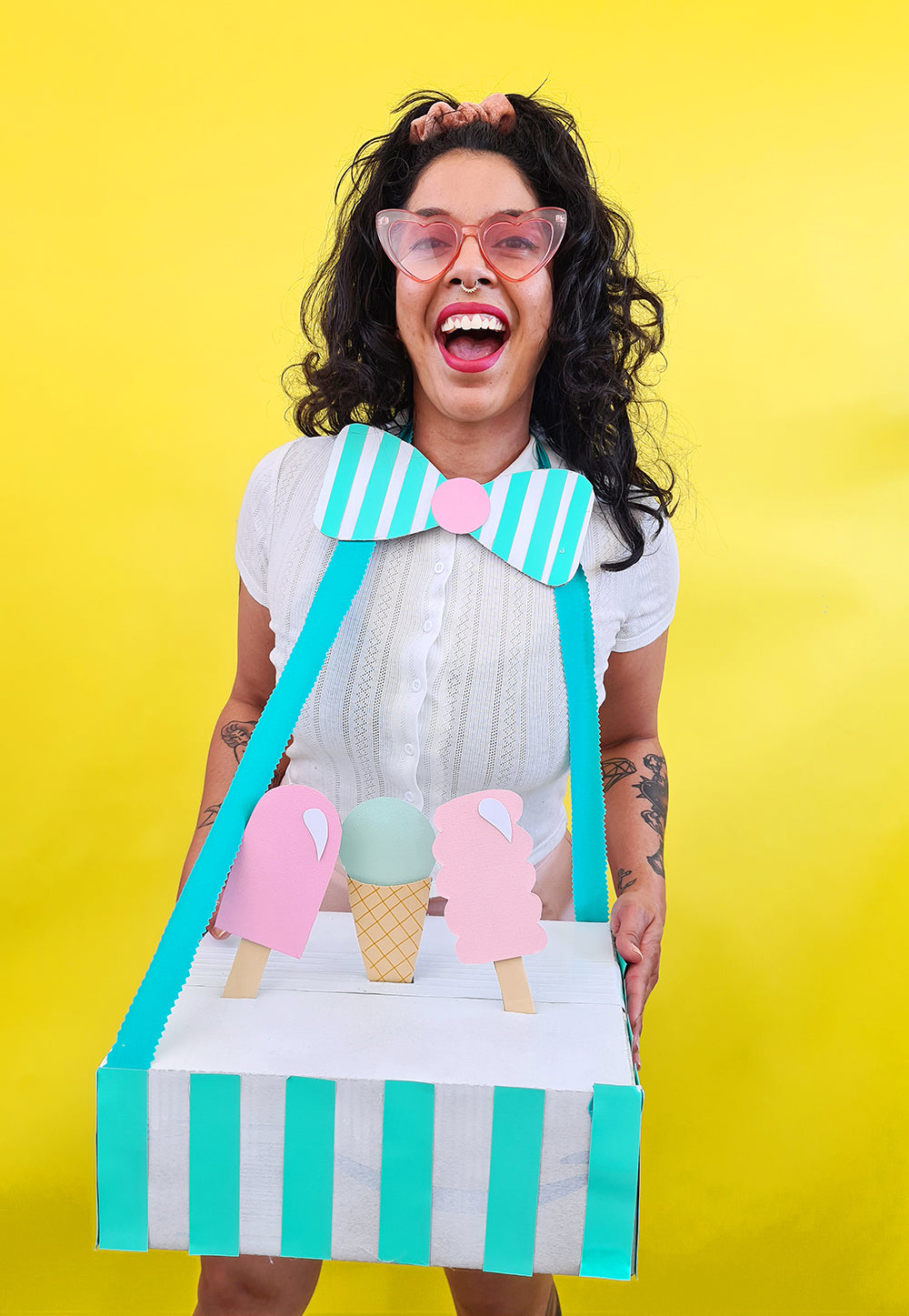 On a yellow background sits a pink, white and green painted 'boxtume' of an icecream truck created by Kitiya Palaskas